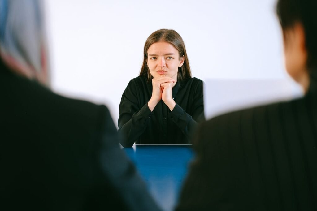 A woman in a job interview facing two people at an office table, focusing intently.