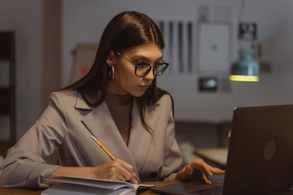 Confident businesswoman working on laptop and taking notes in office setting.
